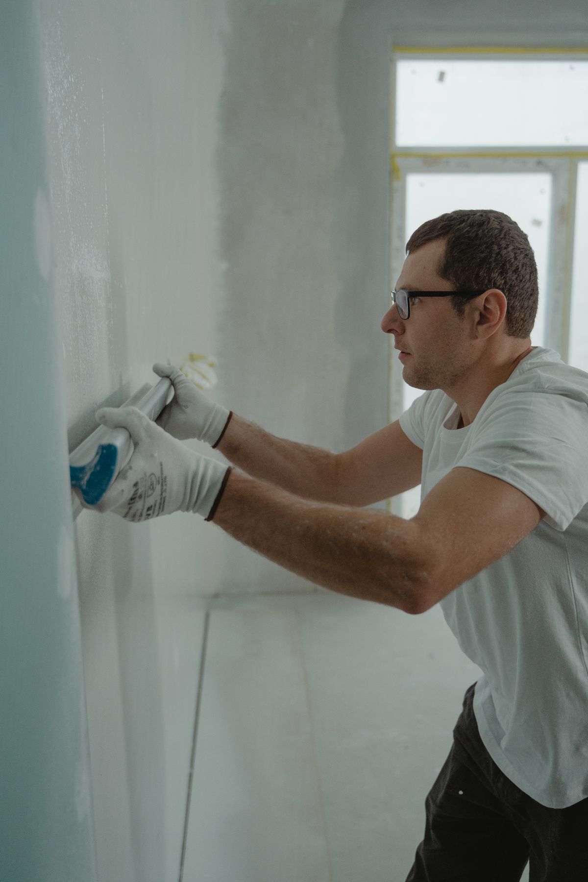 Worker in gloves pressing joint compound onto a wall surface with a finishing tool